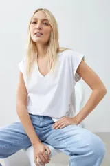 Remera blanca de corte holgado con cuello en V y mangas cortas. Presenta detalle de tela a rayas verticales en los laterales con botones decorativos.