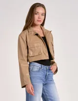 Chaqueta corta color beige de cuero sintético, con cuello clásico, cierre frontal con botones a presión, bolsillos con solapa en el pecho y forro interno a tono.