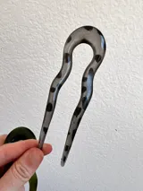 Pinza para el pelo en forma de U, color gris translúcido con manchas negras.