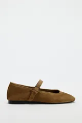 Zapato plano tipo bailarina color marrón de serraje, con escote redondo y cierre mediante hebilla en el empeine.