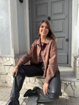 Chaqueta marrón de gamuza con cuello camisero, cierre frontal con botones y bolsillos de parche en el pecho.