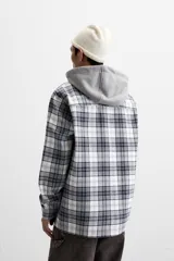 Sobrecamisa relaxed fit de algodón a cuadros azul marino y blanco, con capucha gris combinada a contraste, manga larga con puños abotonados, bolsillos plastrón en el pecho, bolsillos laterales en la cadera y cierre frontal con botones.