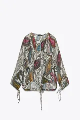 Blusa semitransparente de cuello redondo y manga larga con lazadas ajustables en los puños. Tiene bajo ajustable con lazada y cierre frontal con botones ocultos.