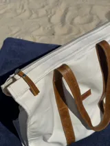 Bolso tipo tote color crudo con asas de cuero marrón.