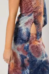 Conjunto de falda larga y top asimétrico con estampado tie-dye en tonos azul, naranja y marrón. El top es de un solo hombro y tiene un collarín con flecos dorados.