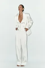 Pantalón blanco de tela satinada, tiro alto, corte ancho y pliegues en la parte delantera y trasera.