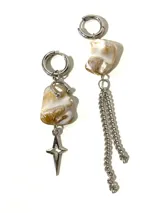 Par de aros asimétricos con argolla de acero quirúrgico. Uno presenta una piedra irregular color crema con detalles marrones y dije de estrella plateada. El otro presenta una piedra similar con cadenas colgantes plateadas.