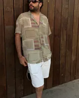 Camisa de manga corta con cuello clásico y estampado geométrico en tonos verde, beige y rojo. Cierre frontal con botones. Corte recto.