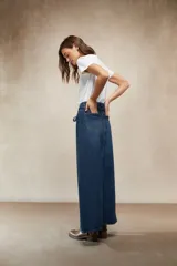 Falda larga de mezclilla color marrón chocolate, de tiro alto con cordón ajustable en la cintura y abertura frontal pronunciada.