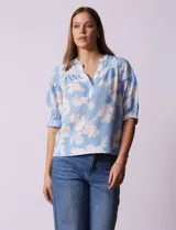 Blusa de gasa estampada con flores blancas sobre fondo celeste, marca Floral & Ivy. Cuello a la base con escote en V. Manga corta con detalle de puño y botón.