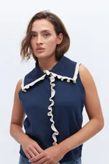 Chaleco de punto sin mangas, color azul marino, con cuello y frente adornados con volados en contraste de color blanco o crudo.