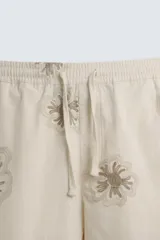 Bermuda regular fit color beige con bordados de flores en tono marrón. Tiene cintura elástica ajustable con cordón, bolsillos laterales y un bolsillo trasero de plastrón.