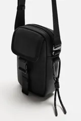 Bandolera vertical negra de acabado engomado con compartimento principal con cierre de cremallera y bolsillo interior plano. Bolsillo frontal con cierre de hebilla de liberación rápida. Asa de hombro ajustable y extraíble.