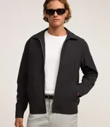 Campera negra de algodón con cuello inglés, cierre con cremallera, manga larga con ajuste fruncido elástico en el bajo trasero y bolsillos laterales.