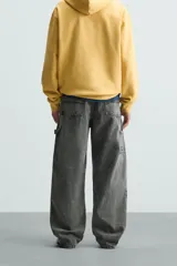Pantalón gris de corte relaxed fit, con cinco bolsillos, efecto lavado, aplicación de tira y bolsillo multifunción en perneras. Cierre frontal con cremallera y botón.