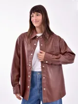 Camisa marrón oscuro de cuero sintético, de corte recto, con cuello camisero, cierre frontal con botones a presión y bolsillo de parche en el pecho.