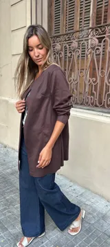Chaqueta tipo blazer sin cuello, color marrón oscuro, de corte recto y largo a la cadera, con mangas tres cuartos y bolsillos frontales.
