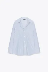 Camisa blanca con rayas verticales azules y detalles de hilo metalizado. Tiene cuello solapa, escote pico, manga larga, bajo asimétrico y cierre frontal con botones.