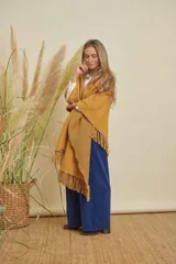 Ruana tejida color mostaza con terminación en flecos de lana y espalda en forma de V.