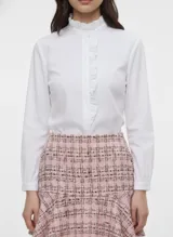 Camisa blanca de manga larga con cuello alto fruncido y tapeta de botones frontal adornada con volantes verticales.