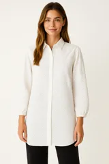 Camisa blanca de algodón con bordado tipo broderie, corte holgado, cuello camisero y mangas 3/4 abullonadas.