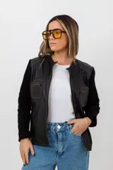 Campera negra con cuerpo de cuero y mangas de tejido de punto. Tiene cuello redondo, cierre frontal con cremallera, dos bolsillos con cremallera en el pecho y costuras decorativas en los hombros.