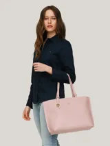 Bolso tipo tote color rosa pálido, con doble asa de hombro y cierre superior con cremallera. Incluye un dije colgante con el logo de la marca y el logo metálico en la parte frontal.