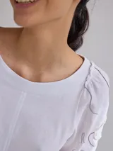Remera gris de algodón con mangas color beige con bordados de líneas en blanco, amarillo y gris.