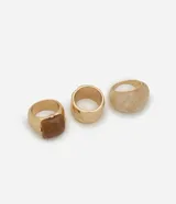 Set de tres anillos con diferentes diseños: uno dorado con textura, uno marrón con forma cuadrada y uno blanco marmolado.