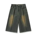 Bermuda de jean estilo baggy, tiro alto con cintura parcialmente elástica y cierre de botón. El lavado es oscuro con un efecto de decoloración horizontal en tono ocre/marrón claro en la parte delantera de las piernas.