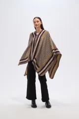 Poncho de tejido grueso con cierre frontal parcial. Presenta un diseño geométrico con bloques de color y patrones a cuadros en tonos marrón oscuro, mostaza, gris y beige.