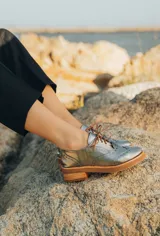 Zapato acordonado color bronce de cuero vacuno con perforaciones decorativas, taco de madera con folia en cuero de 4cm y entre suela de goma de 1,5cm. Horma de punta redonda y cómoda.