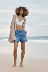 Shorts de denim de tiro medio, color celeste claro con efecto lavado y desgaste sutil. Diseño de cinco bolsillos con cierre frontal de cremallera y botón metálico.