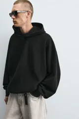 Sudadera negra de tejido con textura acanalada, corte boxy, capucha con cordón ajustable, manga larga con puños acanalados y bajo con elástico.