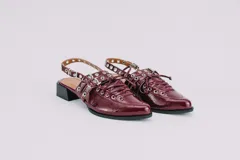 Sueco de cuero negro con cordones, ojales, hebillas y tira trasera regulable con elástico. Tiene taco cuadrado bajo.