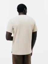 Camiseta color beige con cuello redondo abotonado y mangas cortas.