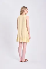 Vestido corto amarillo sin mangas, confeccionado en lino, con cuello con lazo y volados en el ruedo.
