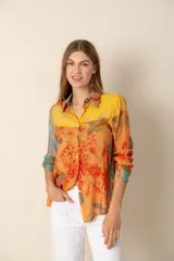 Camisa de manga larga con cuello clásico y botones frontales. Presenta un estampado floral multicolor en tonos amarillo, naranja, celeste y rojo.