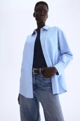 Camisa celeste de algodón Oxford, de corte relajado, con cuello clásico, botones frontales, canesú con trabilla en la espalda, hombros caídos, mangas largas con puños sencillos y bajo redondeado con espalda algo más larga.