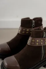 Bota corta de cuero gamuzado color marrón chocolate, con punta cuadrada y suela track. Presenta una correa con hebilla desmontable y cierre lateral con cremallera.