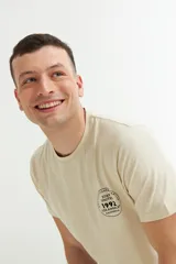 Remera color beige con estampado circular en el pecho con texto en negro.