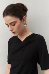 Remera negra de modal de manga corta con cuello asimétrico y detalle de nudo con frunces.