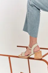 Sandalias de tacón color beige con puntera cuadrada, tiras doradas en el empeine y tobillo, y taco cuadrado.