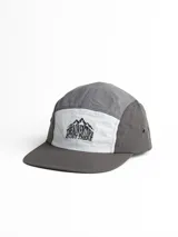 Gorro con visera de cinco paneles, combinado en gris oscuro en la visera y laterales, gris claro en el panel frontal y blanco en el panel central. Estampado frontal con el texto "The Adventure is out there" y un dibujo de montañas.