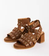 Sandalias de cuero color marrón con plataforma y tacón ancho. Presentan múltiples tiras horizontales con tachas plateadas y pulsera desmontable con hebilla al tobillo.