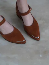 Sandalias de gamuza color marrón con taco bajo y punta cerrada con detalle metálico plateado.