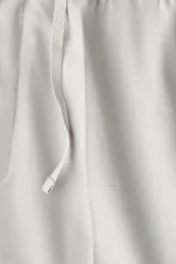 Pantalón de vestir gris claro, de corte slim fit, con cintura elástica y cordón ajustable. Presenta bolsillos laterales y traseros ribeteados, pliegues cosidos y doblez en el bajo.