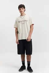 Remera color crema de manga corta con cuello redondo y estampado frontal con la palabra 'Resilience' en tipografía gótica.
