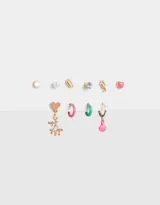 Set de aros dorados con distintos diseños: tachuela, perla, concha, strass, caballito de mar, corazón, coral colgante, argollas rosa y verde, y dije de concha colgante.