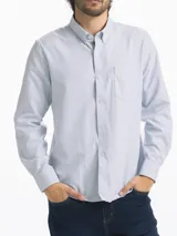 Camisa celeste y blanca a rayas verticales, de manga larga y corte clásico. Tiene cuello abotonado y bolsillo en el pecho.